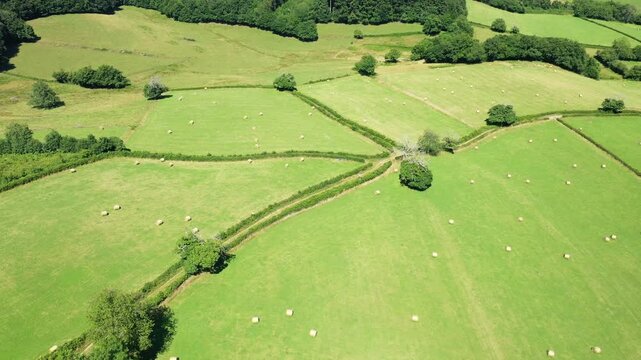 Drone shot of green fields with hay bales and hedgerows in the Morvan countryside, France, on a sunny summer day.
