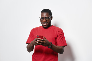 African American man with dark skin wearing glasses and red t shirt smiling while using smartphone...