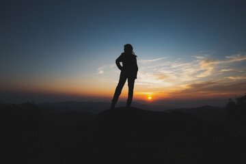 Hopeful silhouette of confident woman standing on mountain at sunset. outdoor scene features dramatic sky with sun on horizon, creating peaceful mood
