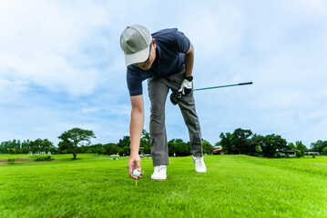 Fototapeta premium Professional golfer placing golf ball on a tee on lush green golf course. 