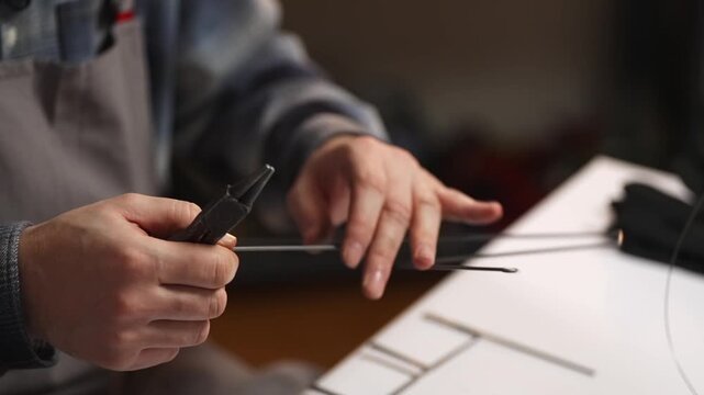 Close up of artisan using pliers to bend steel wire in traditional Slovak wire craft workshop. Drotarstvo handmade metal art process and skilled craftsmanship concept.