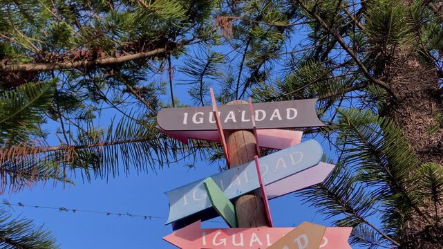 Multicolored wooden signs presenting the word igualdad in different directions, symbolizing equality and diverse paths under blue sky