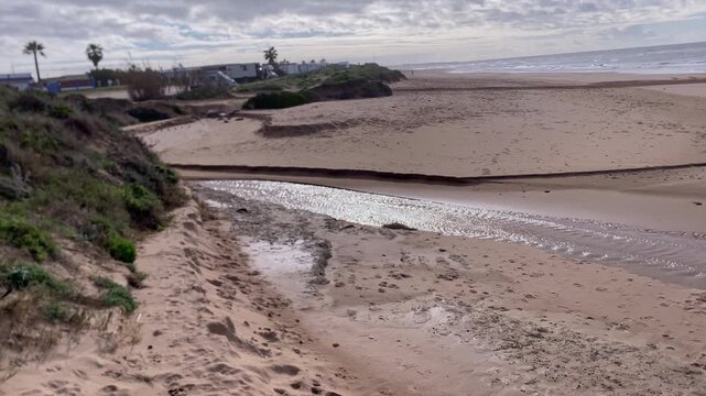 Sandy Rota beach landscape showing a small stream flowing across the sand into the Atlantic Ocean under a blue sky
