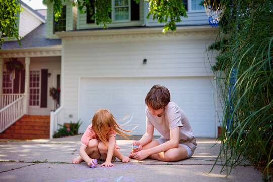 Brother and Little Sister Playing Tic Tac Toe Game with Chalk on Driveway &mdash; Happy Sibling Bonding and Outdoor Childhood Play at Home in Suburban Neighborhood