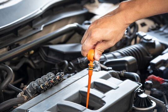 Hand of technician checking the oil level of a modern car engine using a dipstick for regular vehicle maintenance service and preventive automotive care in a garage. concept car
