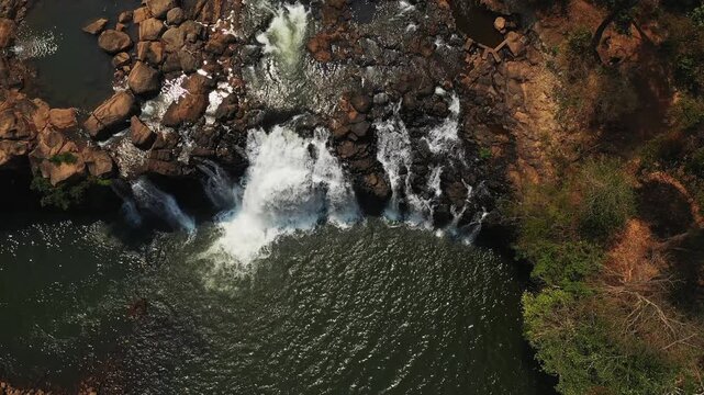 Drone shot of Tad Lo waterfall cascading over rocks into a river, surrounded by lush greenery in southern Laos.