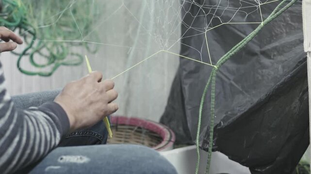 Authentic video of a fisherman carefully repairing fishing nets by hand. Traditional fishing work requiring patience and skill. Real camera capture, not AI generated.
