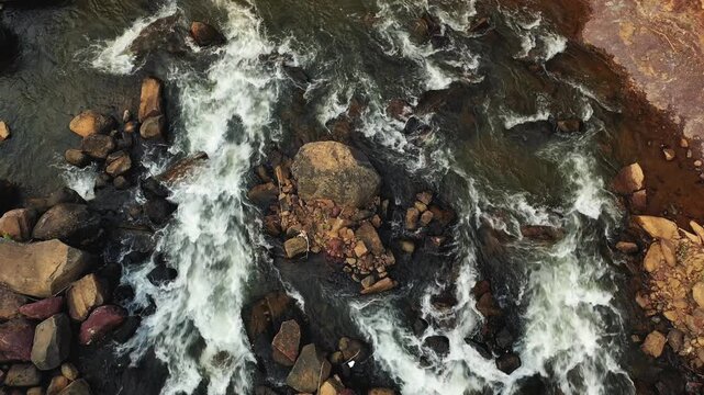 Dynamic aerial shot of river rapids flowing over rocks in Tad Lo, Laos. Natural water movement and rugged stones create a dramatic landscape scene.