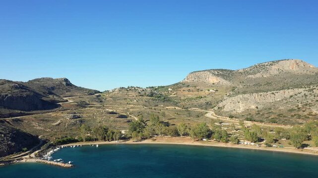 Aerial view of Paralia Karathona beach with turquoise water, lush greenery, and rocky hills near Nauplie, Greece, under a clear blue sky.