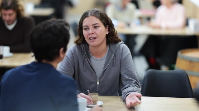 Young couple met in the afternoon in a coffee shop, ordered coffee and chat. Guy and young woman on a date in a cafeteria