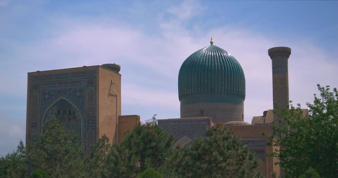 Wide cinematic view of historic tiled dome and minaret skyline rising above garden trees with ornate mosaic facades clean blue sky calm cultural landmark cityscape in 4k readable silhouettes
