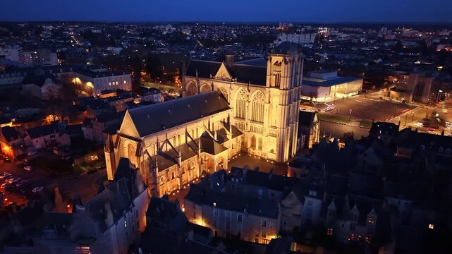 Night drone panning shot behind Saint-Julien Cathedral in Le Mans, illuminated in warm light with the historic city glowing in the background. France