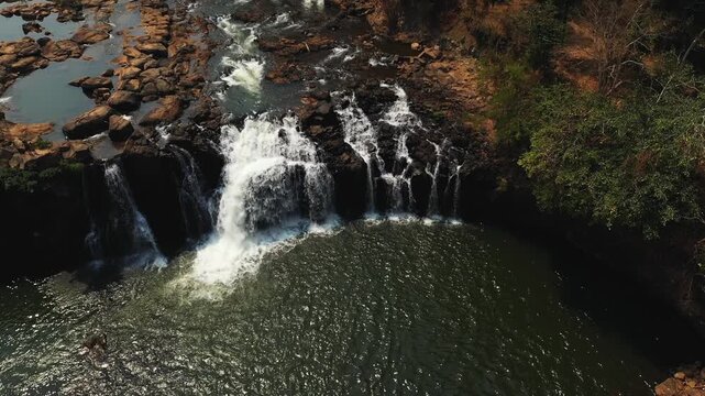 Drone shot of Tad Lo waterfall cascading over rocks into a tranquil pool, surrounded by lush greenery in southern Laos.