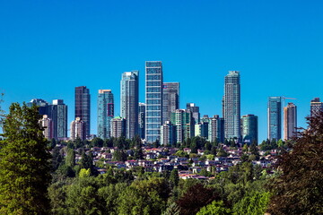 Obraz premium A residential district in Burnaby, with high rise buildings on top of a hill and private homes below, surrounded by green trees against a blue sky