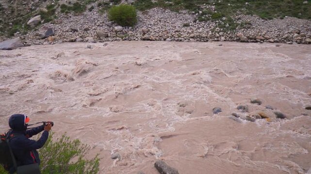 Landscape shot of flooded Chenab river during the monsoon season with a defocused man taking videos of it with camera as seen in Lahaul, Himachal Pradesh, India. Monsoon river background.