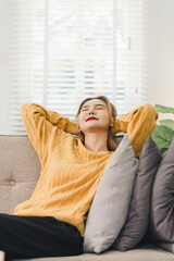 Fototapeta premium Calm young asian woman relaxing on comfortable sofa in living room enjoying peaceful lifestyle stretching arms with happy smile