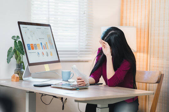 Stressed woman suffering headache and tired business burnout facing financial problem with graph. She feels overwhelmed by heavy debt home office
