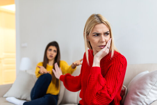 Two women having an argument on the sofa. Young female ignoring her friend after a conflict. Relationship problems, friendship crisis, social distance and communication difficulties concept.