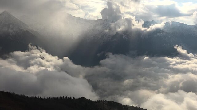 Alps mountain peaks rise above cloud sea as sunrays pierce mist, cinematic landscape view. Swiss range summits overlook overcast layer, god rays through vapor, breathtaking highland vista.