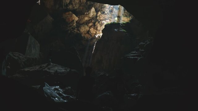 God rays illuminate majestic Laos waterfall flowing through a dark, mysterious, ancient underground cave entrance