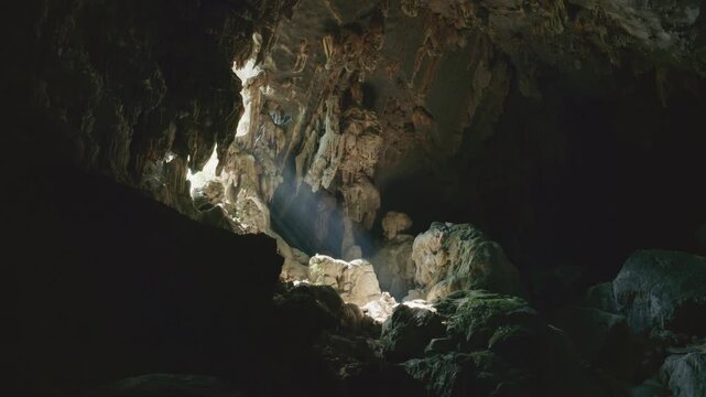 Underground cavern interior with mystical sunbeams illuminating the rock formations and stalactites in dark cave in Laos
