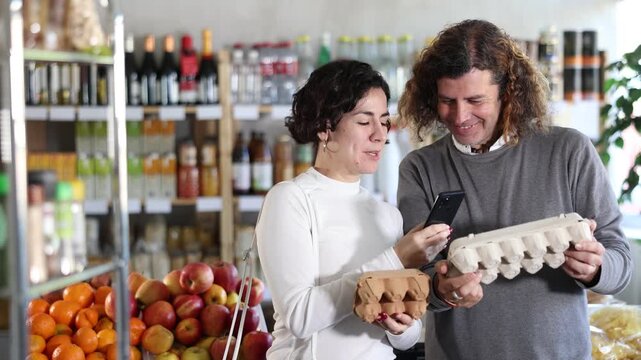 Man and a woman scan the barcode on an egg package on their phone and pay using an online application on their phone. Buyers use modern online payment methods. High quality 4k footage