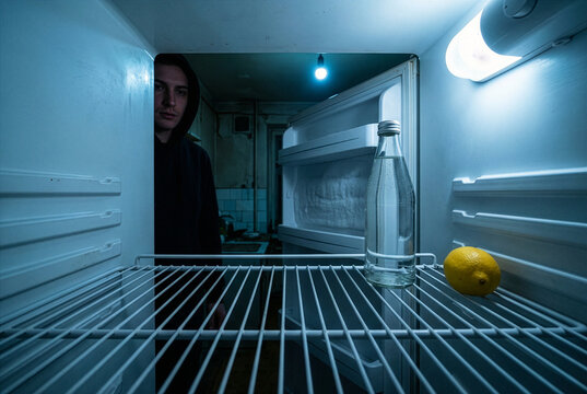 Man staring into an almost empty refrigerator with only a lemon and water bottle inside