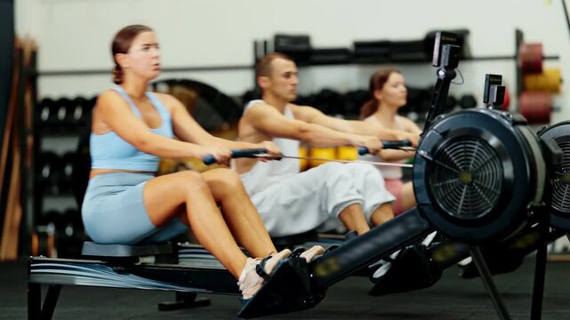 Young woman in sportswear training on rowing machine in gym