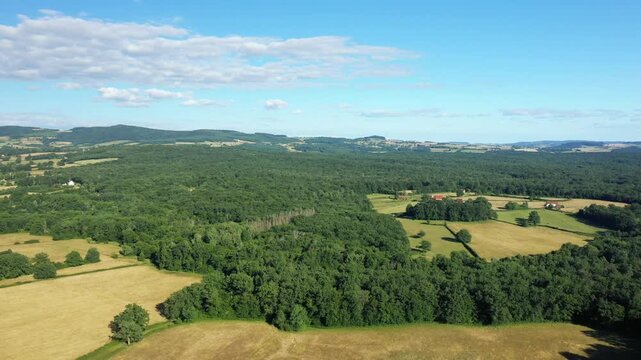 Drone shot of lush green forests and patchwork fields in the Morvan countryside under a blue sky. Scenic rural landscape with rolling hills and scattered farmhouses.