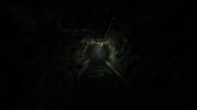 narrow utility corridor lined with service pipes and sensors, dim glow highlights wet rock and metal seams, maintenance access route suggests night shift
