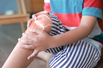 Little boy suffering from knee joint pain with red x-ray bone graphic overlay, child touching leg feeling ache from injury, growing pains, inflammation or accident while playing at home.