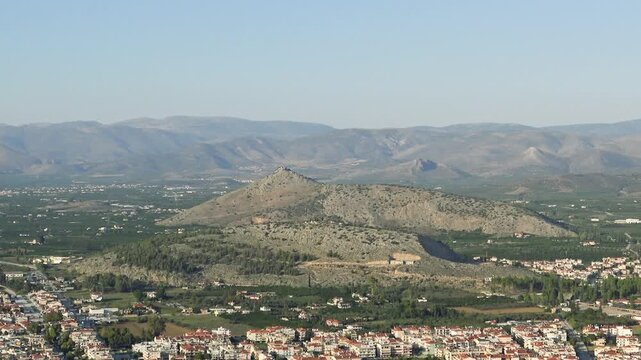 Wide panoramic landscape of rocky hills and green valley near Nauplie, Greece, with distant mountains under a clear sky.