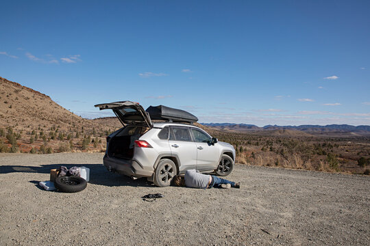 Man lying on the ground in remote outback Australia preparing to fix a flat tyre with a view