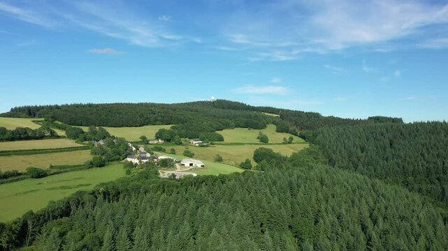 Scenic aerial shot of rolling green hills, forests, and rural farmland in the Morvan region under a blue sky. Tranquil summer countryside with scattered farm buildings and dense woodland.