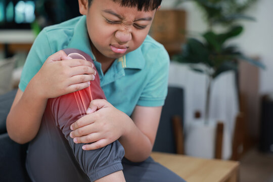 Little boy suffering from knee joint pain with red x-ray bone graphic overlay, child touching leg feeling ache from injury, growing pains, inflammation or accident while playing at home.