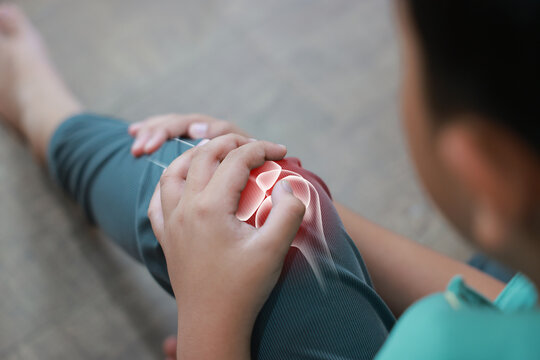 Little boy suffering from knee joint pain with red x-ray bone graphic overlay, child touching leg feeling ache from injury, growing pains, inflammation or accident while playing at home.