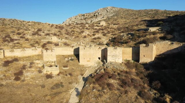 Aerial view of the historic stone ruins of Acrocorinth fortress set on a dry, rocky hillside under clear blue sky in Greece.