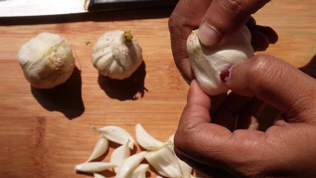 person peeling cloves from a bulb of garlic