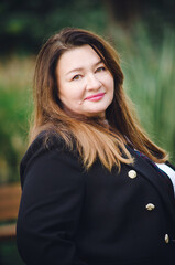 A beautiful middle-aged woman in a business suit smiles happily on the street. Vertical photo.