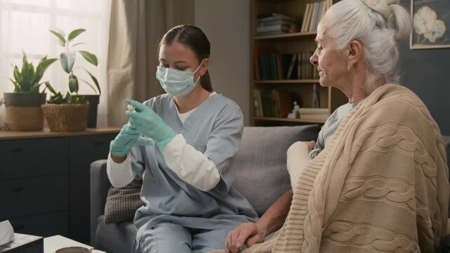 Tilt up view of young nurse filling syringe with medicine, cleansing skin of sick senior lady in preparation and giving shoulder injection to her during home care visit