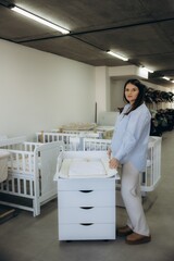 Obraz premium Pregnant woman checking changing table in baby shop