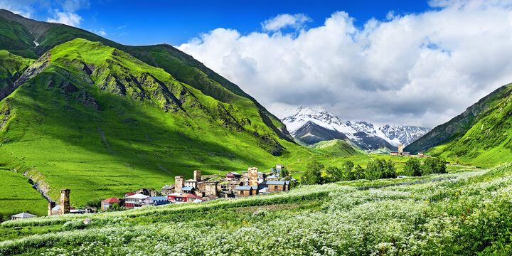 The mountain village of Ushguli (Zhibiani) stretches along the slopes of the Greater Caucasus, Georgia. In the distance, the majestic peak of Shkhara watches over the village, fading into the clouds.