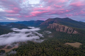 Drone shot of a mountainous landscape at dawn, covered in fog, with pink clouds