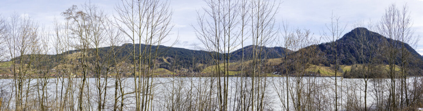 The eastern shore of Lake Schliersee in Upper Bavaria, seen from tree-lined western trail. The town at the foot of the slopes of the Schliesberg, followed by the Breitenberg and Hirschg&ouml;hrkopf