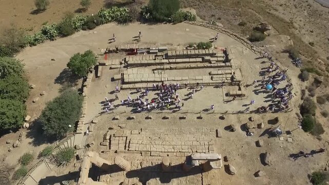 Aerial top-down view of Temple of Concordia at Valley of the Temples, Agrigento, Sicily, Italy, ancient Doric columns with tourists exploring the ruins in dry landscape.