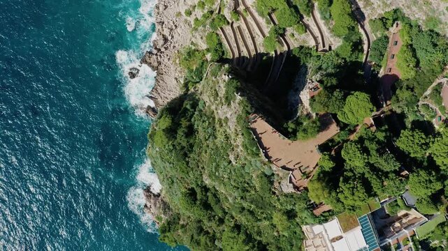 Aerial Top Down View with Terrace in Gardens of Augustus and Walking Path of Via Krupp in Capri Island. Green Vegetation and Turquoise Sea Water Waves Crashing on the Rocky Limestone Cliffs.