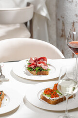 Gourmet open sandwiches topped with salmon cream cheese and prosciutto served on white table in restaurant