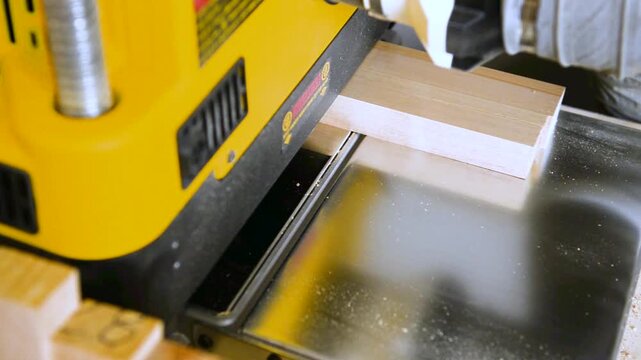 A wood plate passing through the thickness planer machine in a carpentry workshop. Woodworking process, furniture preparation, handmade craftsmanship, carpentry studio.