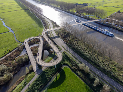 Aerial view of the looping Liniebrug bridge curving dramatically over the watery landscape, a modern marvel against the backdrop of green fields, Liniebrug, Utrecht, Netherlands.