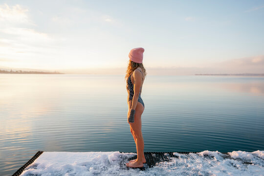 Woman standing on snowy dock after winter swim in lake at sunset
